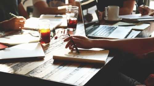 A group of people working around a table with laptops, notepads and drinks