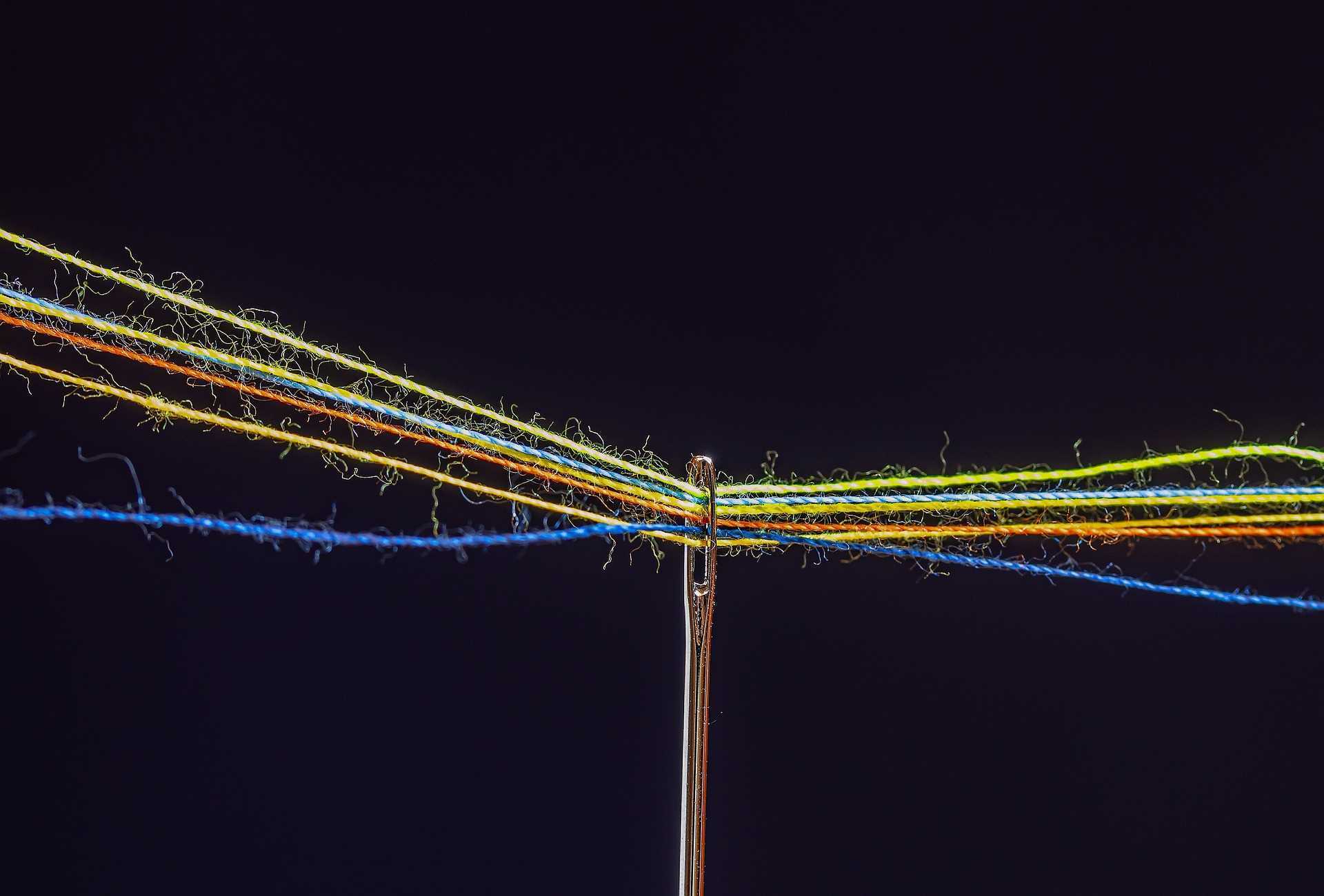 A photo of lots of coloured threads running through the eye of a needle