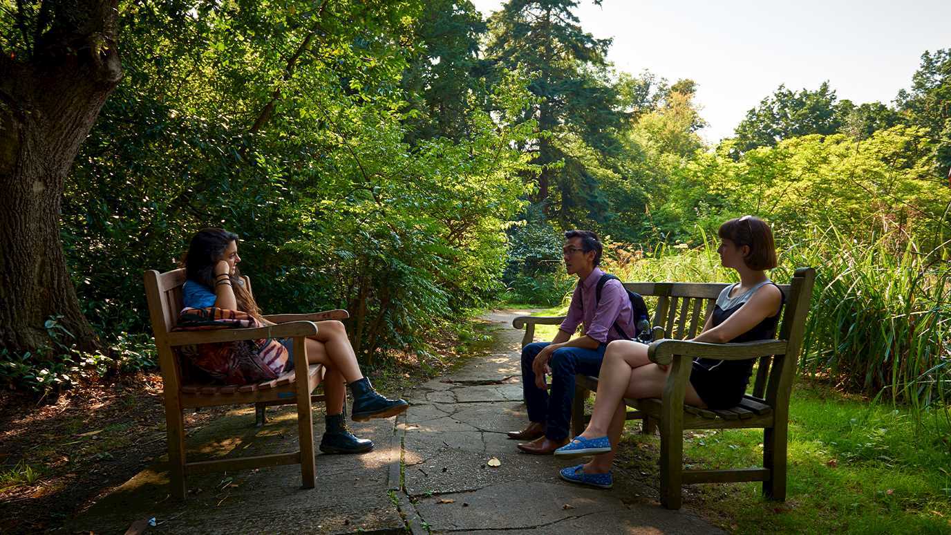 Three people sat on benches in a garden area on the Egham campus.