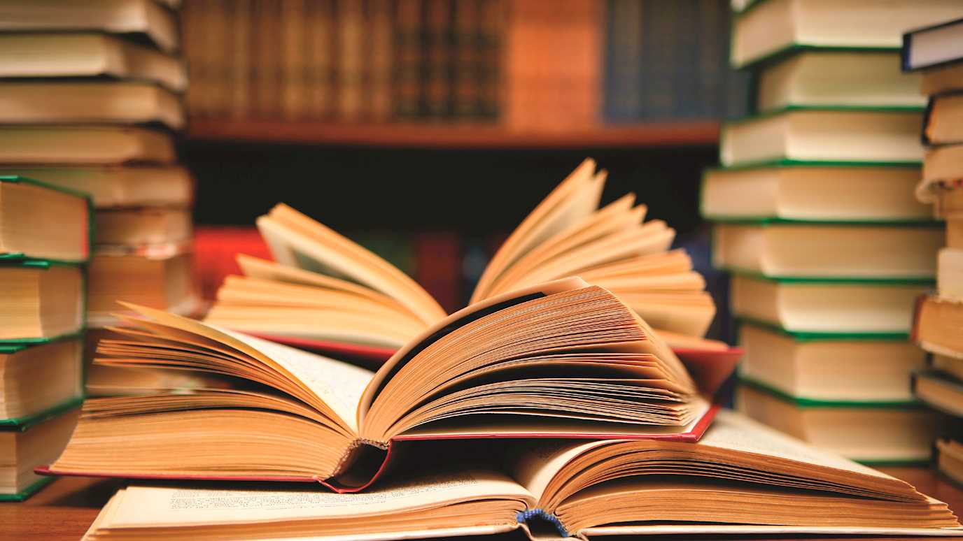 Piles of books on a table in a library - English